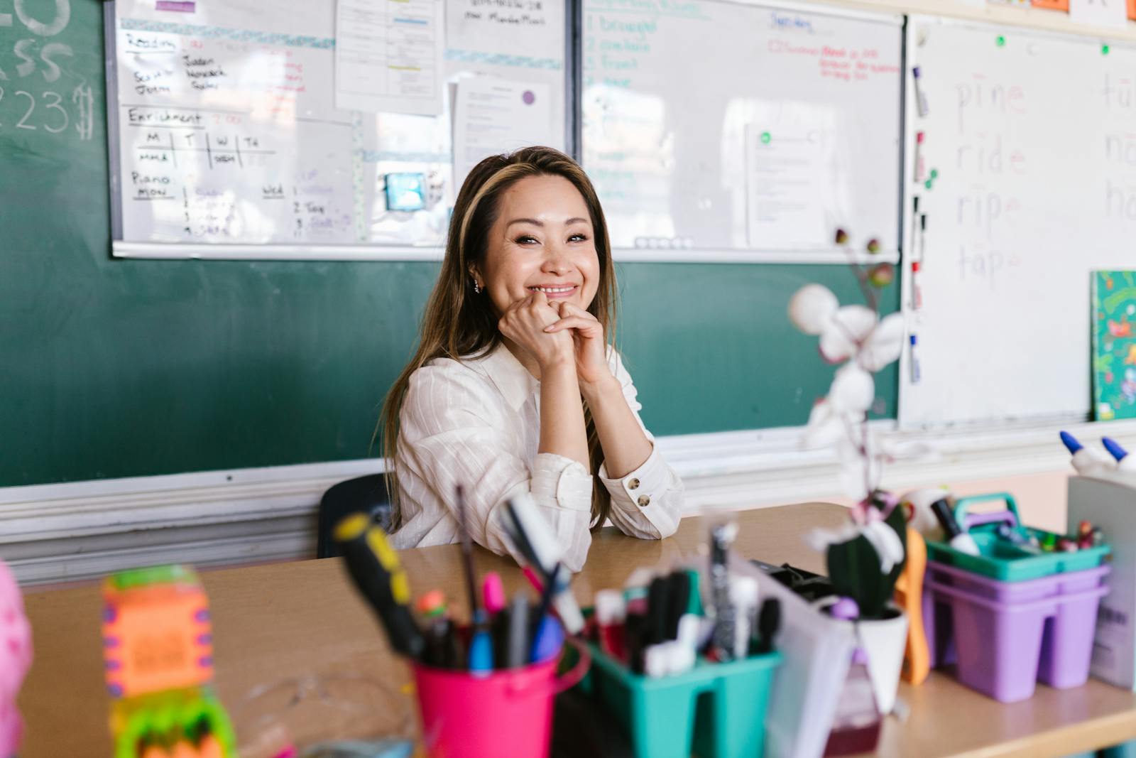 Photo by RDNE Stock project Cheerful teacher sitting at a desk in a bright classroom with school supplies.
